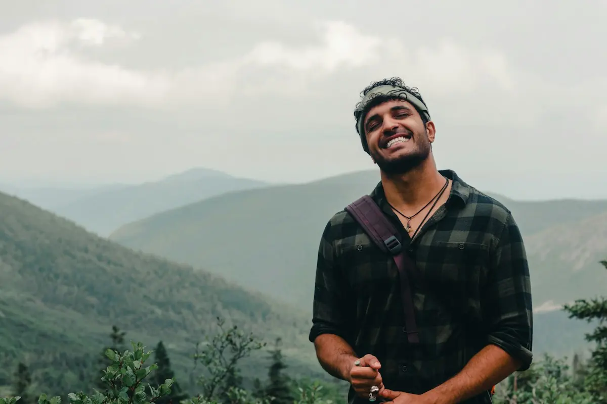 A man laughs on a hillside above misty green mountains.